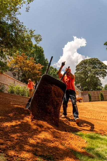 Workers unloading orange-brown material at a construction site under a bright blue sky