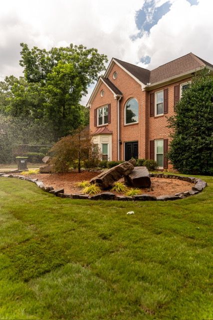 Brick house with a landscaped front yard, green lawn, and rock garden under cloudy skies