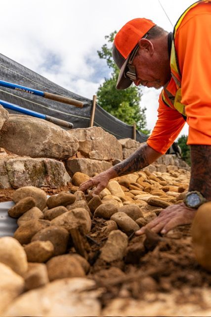 Worker in orange safety gear placing stones at a construction site