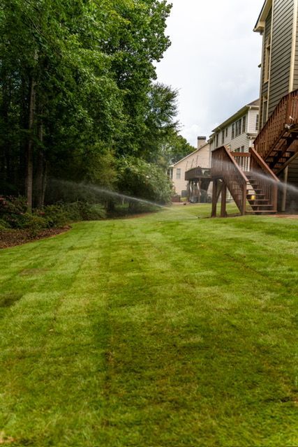 Green lawn beside apartment buildings with trees and a sprinkler spraying water