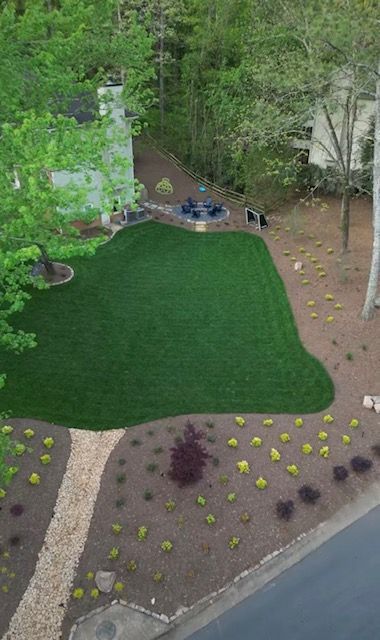 Aerial view of a green backyard lawn bordered by trees, mulch beds, and a paved driveway.