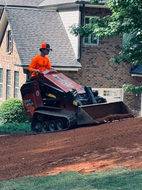 Worker operating a red tracked skid steer spreading dirt in a residential yard.