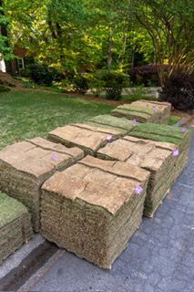Stacks of sod rolls beside a paved path in a landscaped garden area