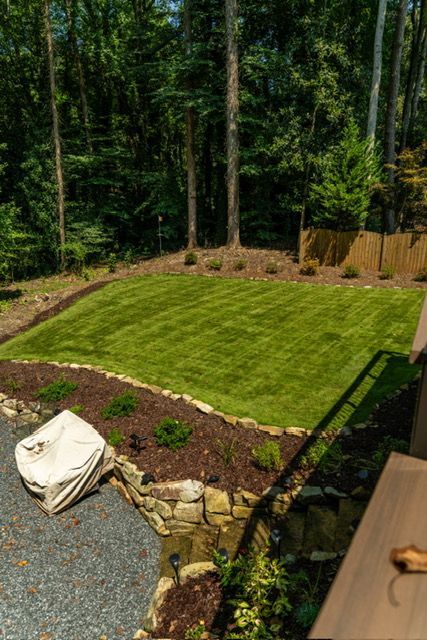 Backyard with a freshly laid green lawn bordered by gravel, stone, and dense trees