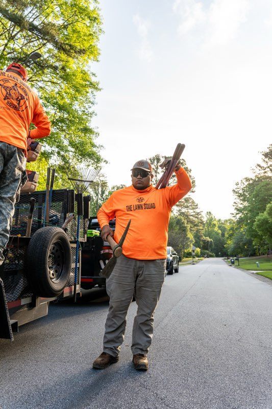 Worker in orange shirt waving beside a truck on a tree-lined road