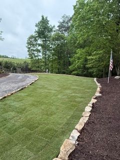 Freshly sodded green lawn bordered by mulch and rocks in a wooded yard with an American flag