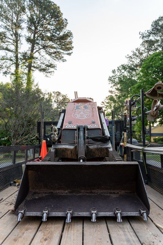 Front loader tractor with raised bucket on a trailer, outdoors among trees and fencing