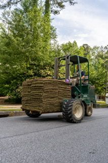 Forklift carrying a large stack of sod along a tree-lined road
