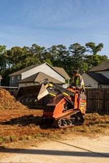 Construction worker operating an orange skid-steer loader at a residential construction site.