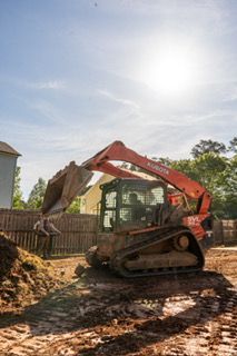 Red excavator on tracks working in a muddy backyard under a bright sky