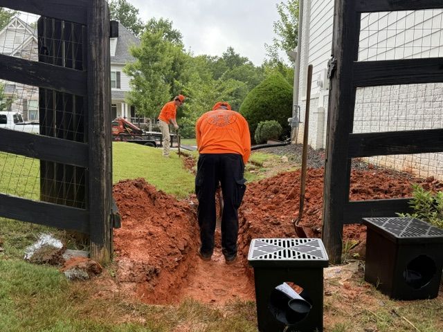 Workers in orange vests digging a trench in a backyard beside a house