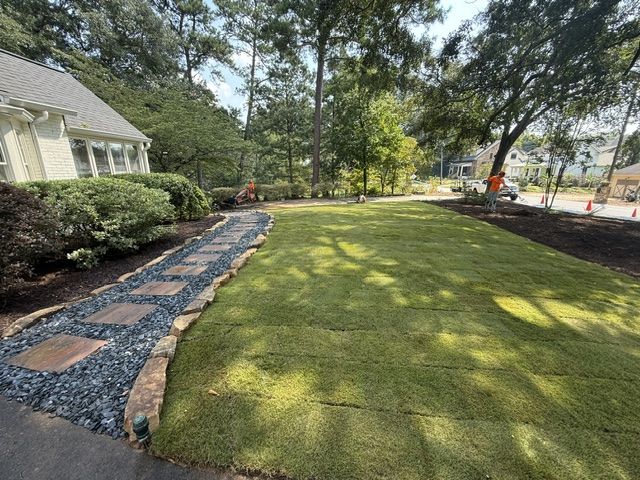 Landscaped front yard with winding gravel path, stone border, mulch beds, and trees