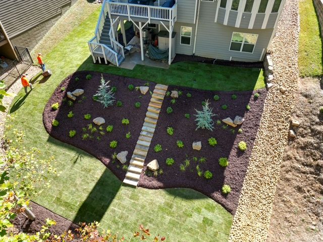 Backyard landscaping with dark mulch, stepping stones, and small shrubs beside a house and deck