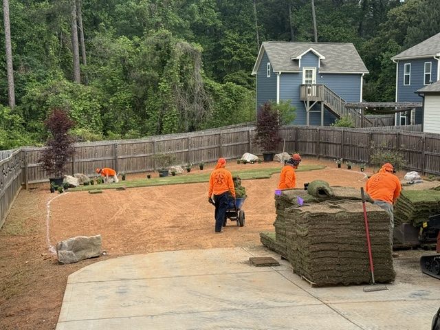 Workers in orange jackets laying sod in a fenced backyard under construction