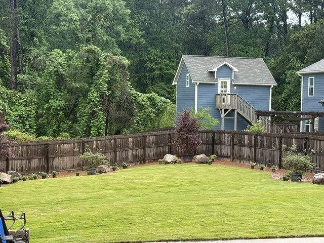 Backyard lawn with a wooden fence, flower beds, and two blue houses behind trees