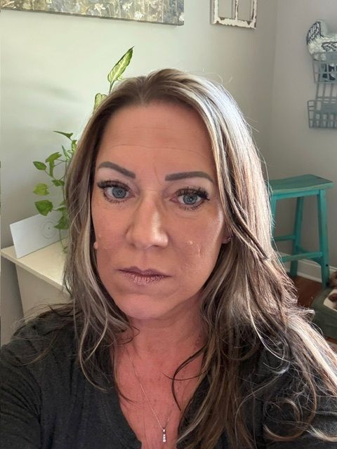 Close-up selfie in a room, showing a woman with long wavy hair and neutral expression.