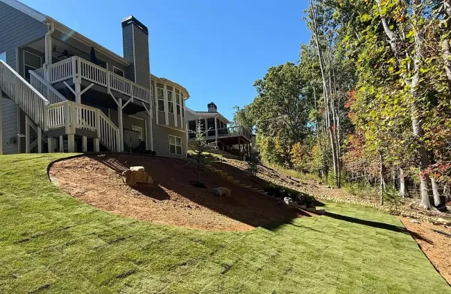 Backyard with a house, sloped green lawn, and landscaped mulch bed under clear blue sky