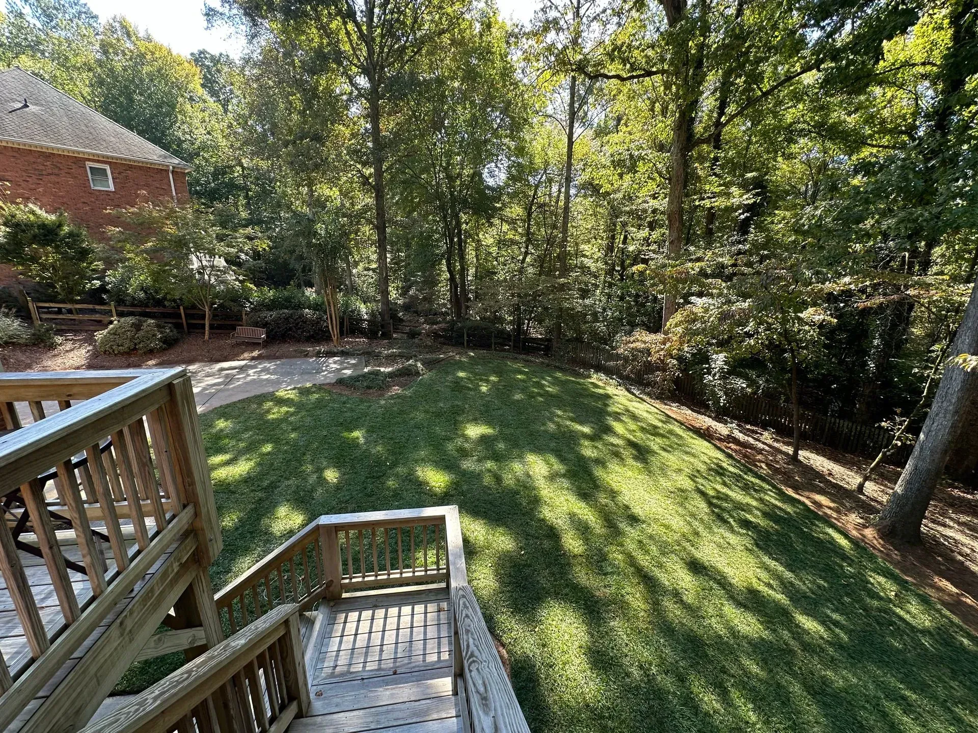 Wooden deck overlooking a grassy backyard with trees and a brick house.