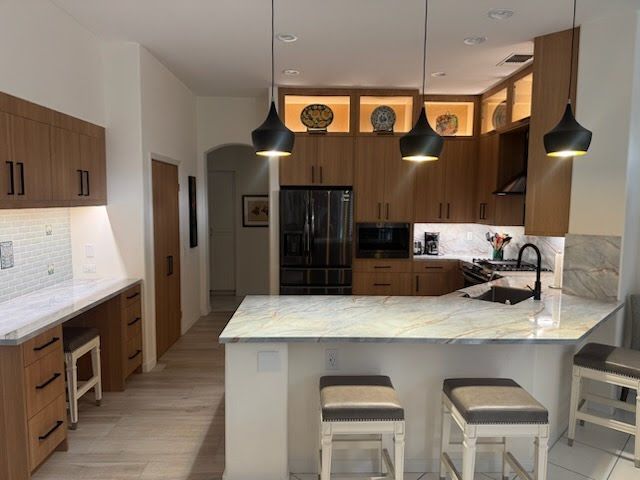 Modern kitchen with wood cabinets, black appliances, white countertops, and pendant lights.