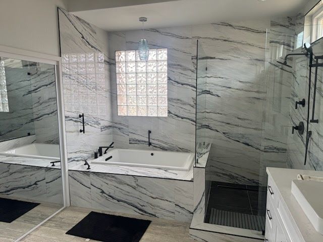 Modern bathroom with marble-look walls, glass shower, bathtub, and black fixtures.