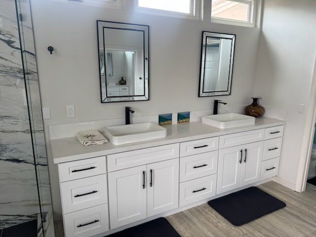 White bathroom vanity with two sinks, black fixtures, mirrors, and cabinetry.