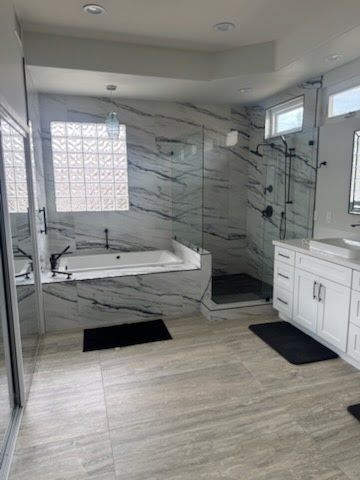Modern bathroom with marble walls, glass shower, white vanity, and tub.