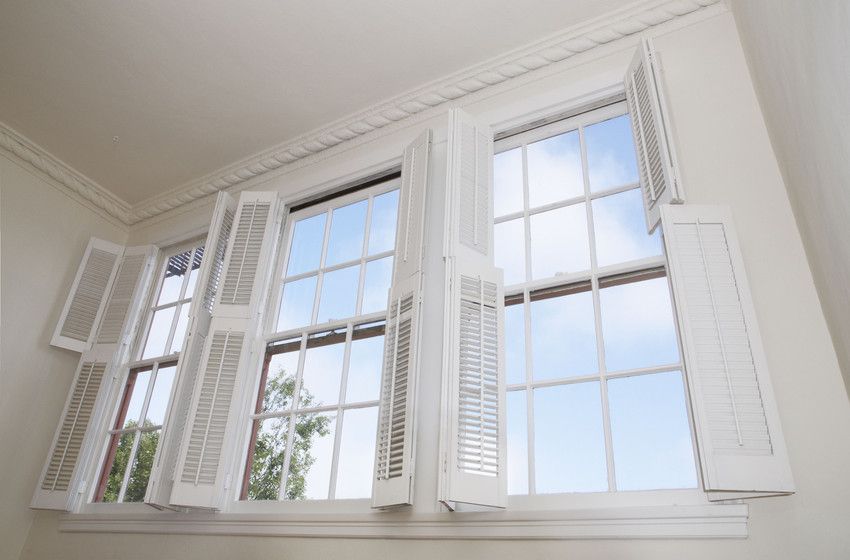 A window with shutters open and a blue sky behind it.