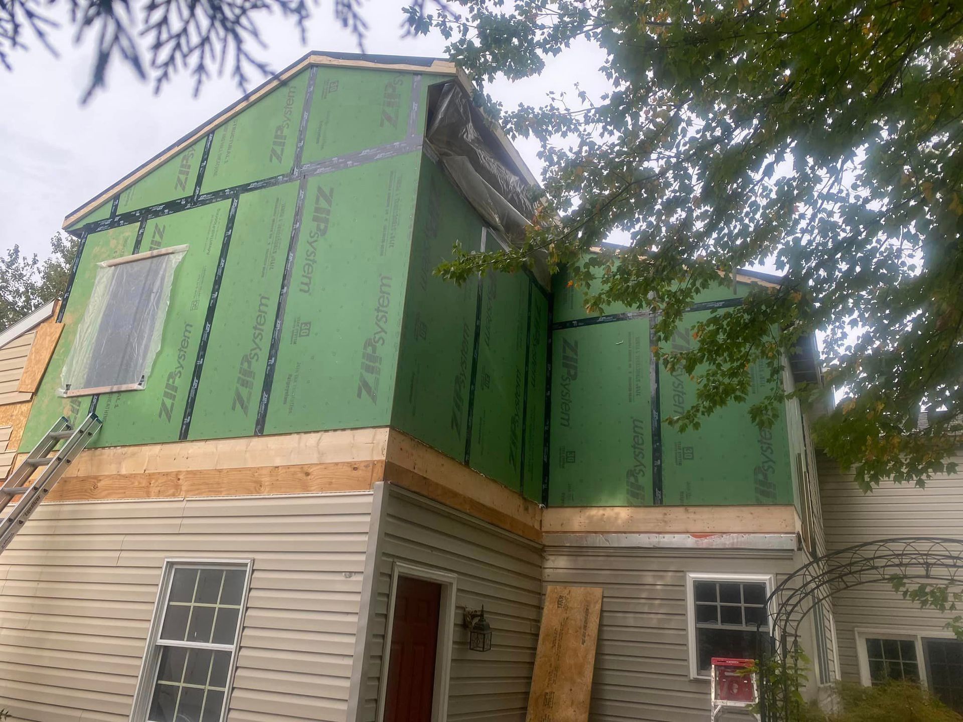A house is being remodeled with green siding and a ladder