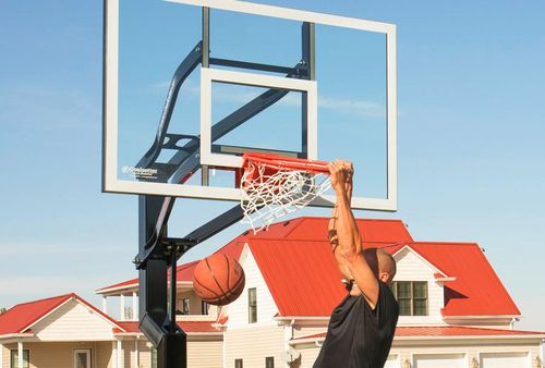 Basketball player dunking on an outdoor court with red-roofed houses in the background
