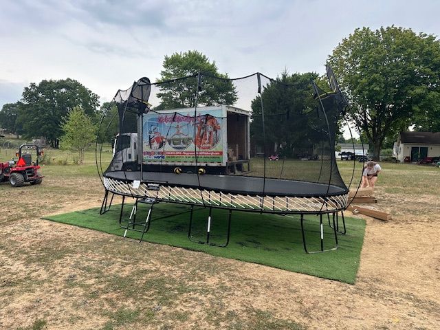 Backyard trampoline with safety net on green turf, beside a banner and trees