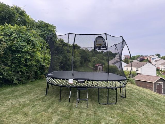Trampoline with safety net on a grassy backyard lawn beside bushes and houses