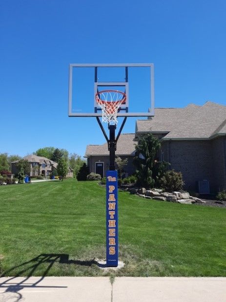 Portable basketball hoop in a suburban driveway, with green lawn and houses under a clear blue sky