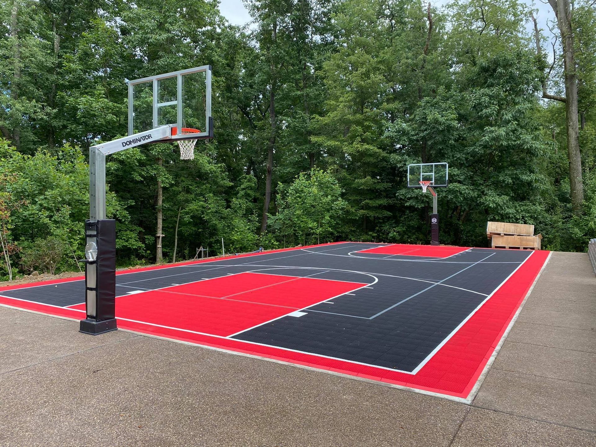 Outdoor basketball court with red and black surface, two hoops, surrounded by trees