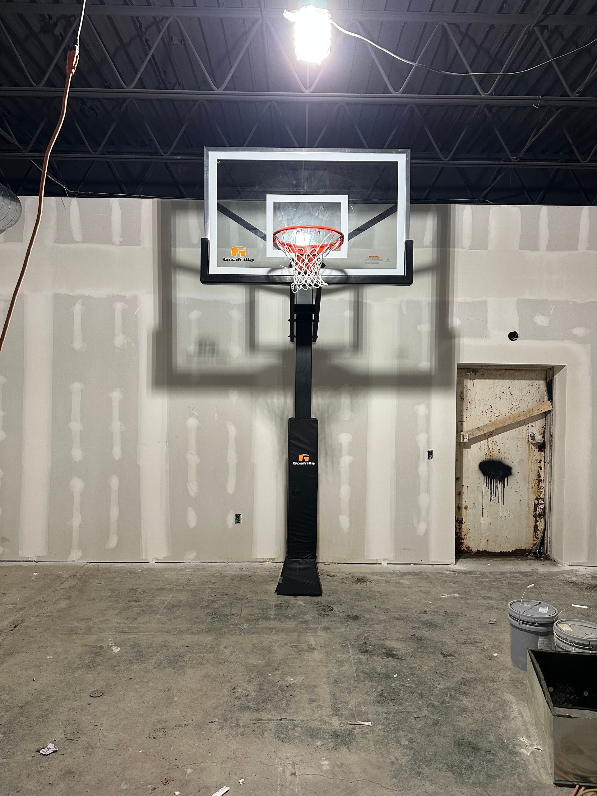 Indoor basketball hoop in an unfinished warehouse with concrete floor and exposed ceiling beams