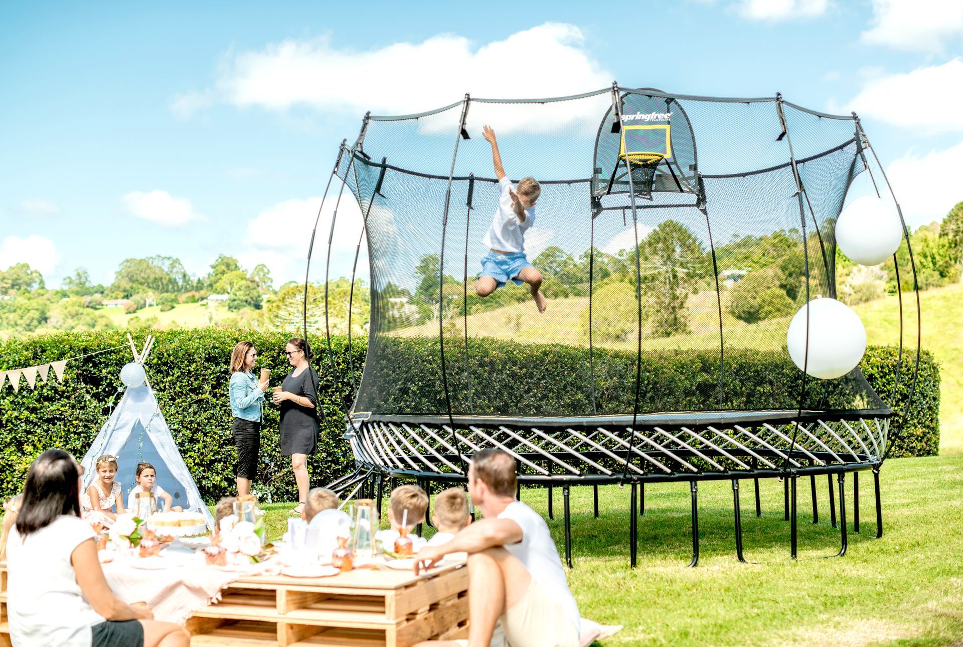 Children playing in a backyard trampoline and picnic scene on a sunny day
