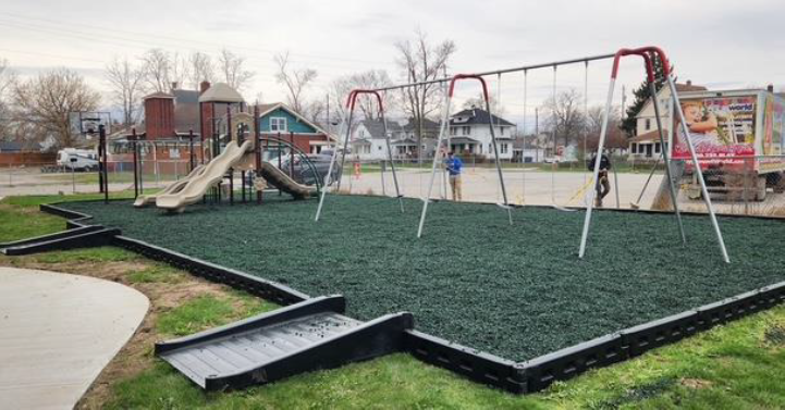 Empty playground with swings and slide on wet green turf in a park.