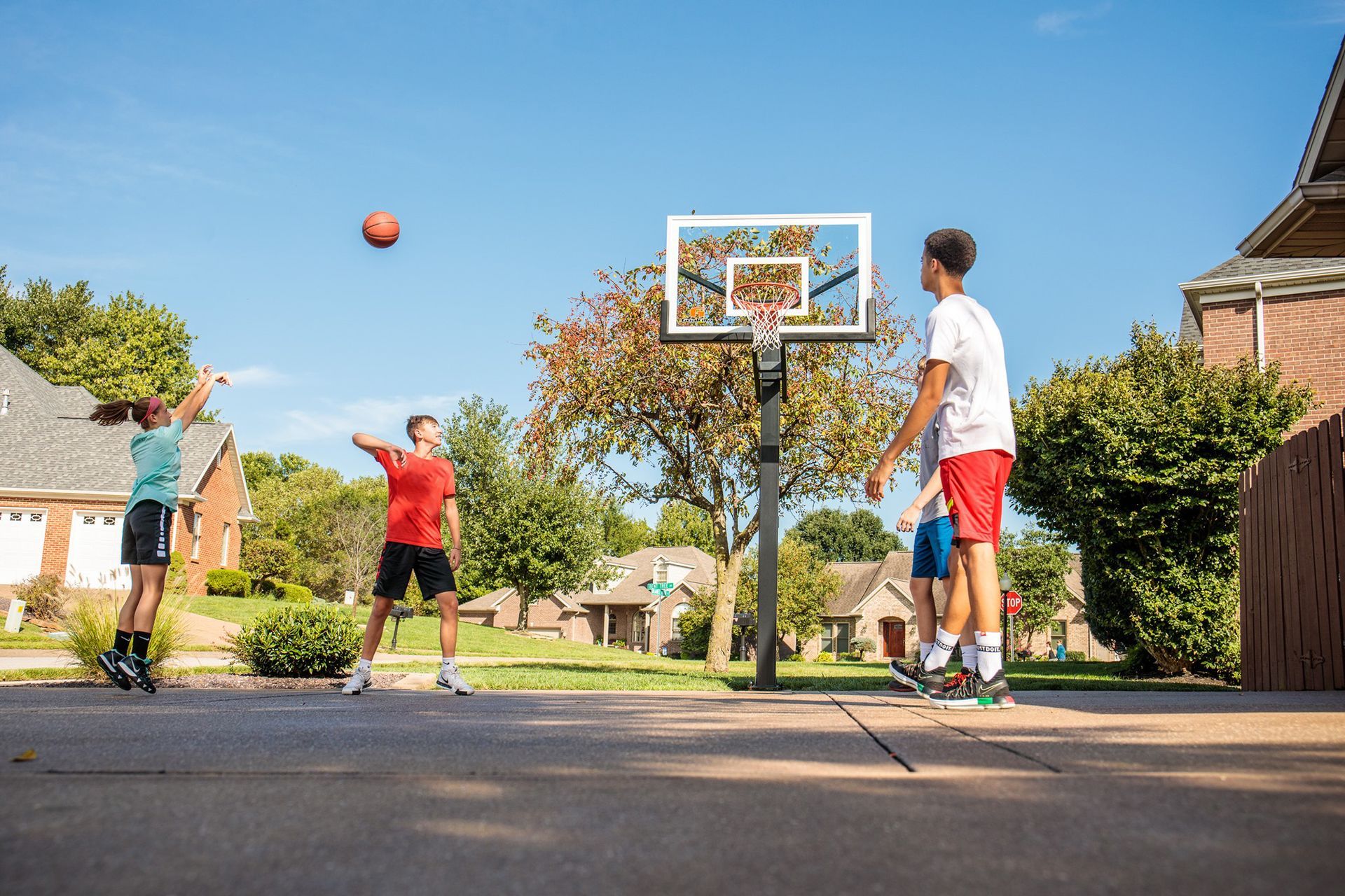 Kids playing basketball on a driveway with a hoop and ball in a sunny neighborhood