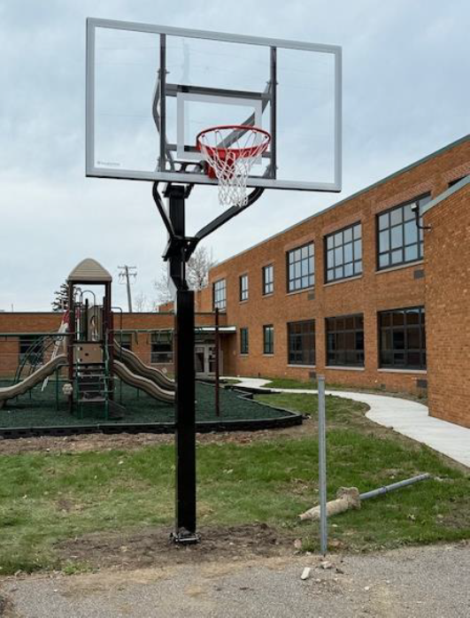 Basketball hoop beside a playground and brick school building on a cloudy day