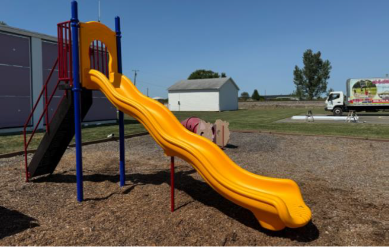 Yellow playground slide on a mulch-covered play area under a clear blue sky