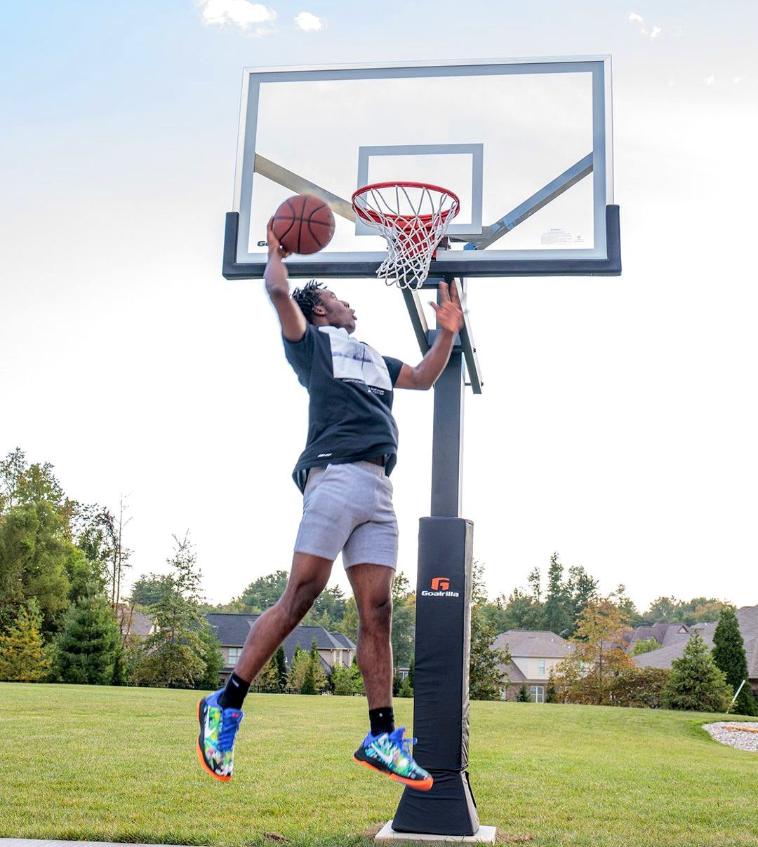 Man jumping for a basketball layup at an outdoor hoop on a grassy court.