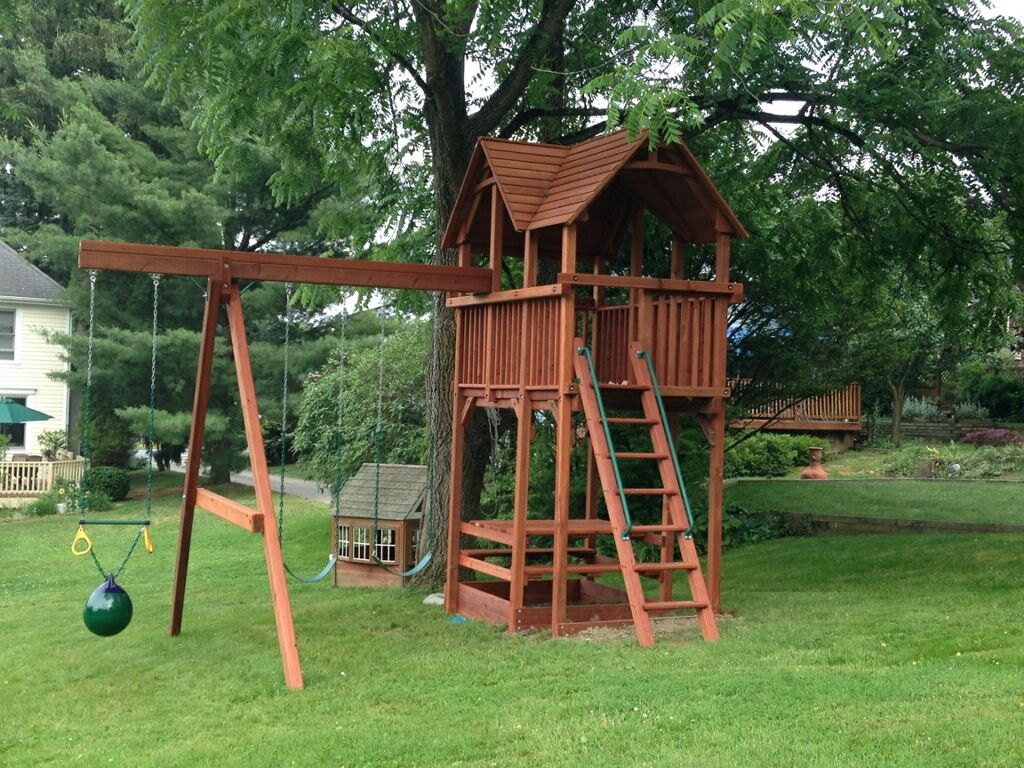Backyard wooden playset with swing, climbing ladder, and treehouse fort on a grassy lawn.