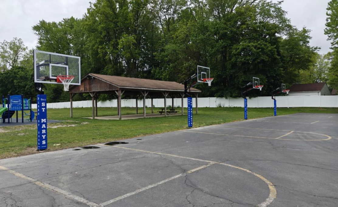 Outdoor basketball court with two hoops, a covered bench area, and trees in the background