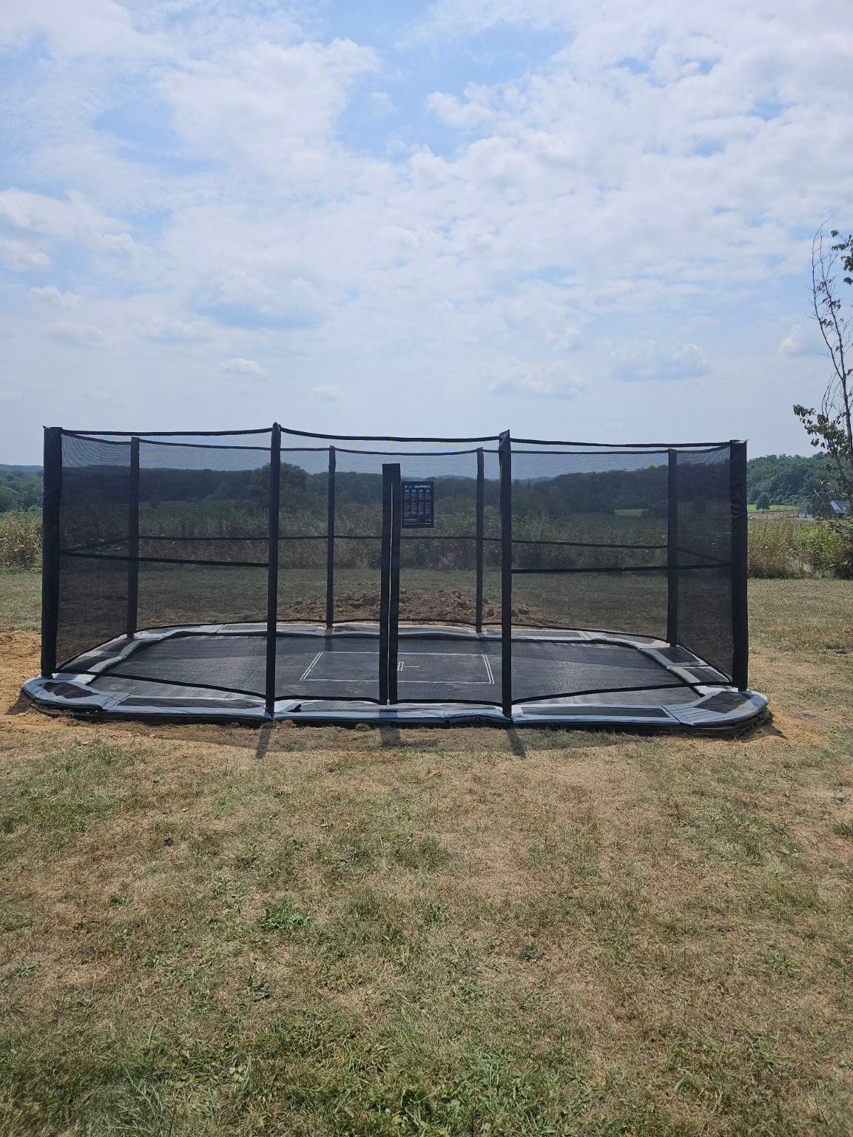 Black-framed trampoline with safety net in a grassy field under a cloudy sky