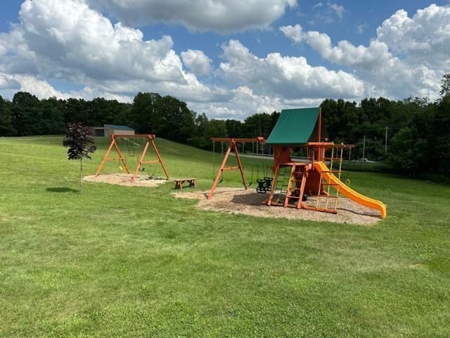 Empty playground with swings and orange slide on a grassy field under a cloudy sky