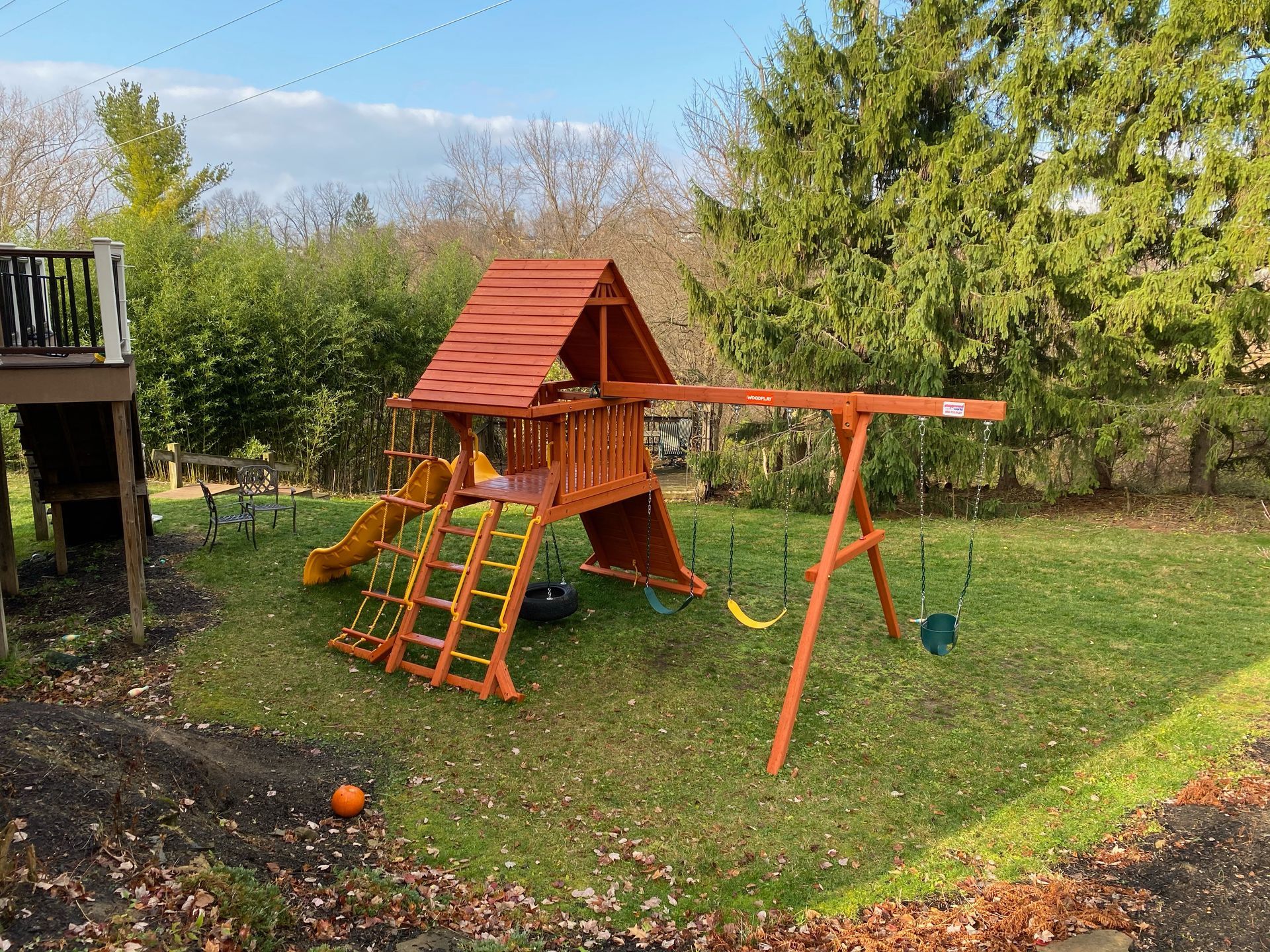 Backyard wooden playset with slide, climbing wall, and swings on a grassy lawn