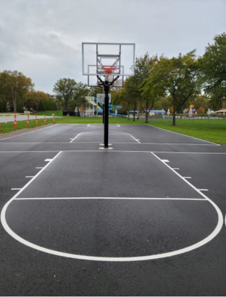 Empty outdoor basketball court with a hoop on a wet, overcast day.