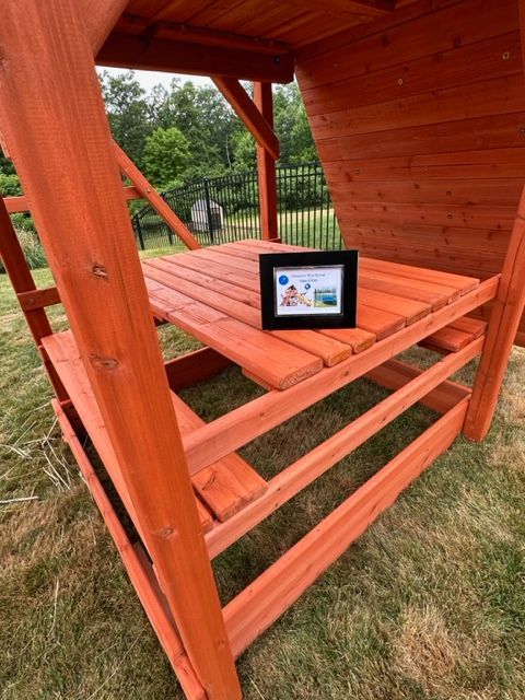 Orange wooden playhouse with a tablet on the bench inside, seen from a grassy yard
