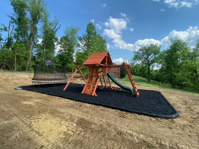 Wooden playground structure with swings and slide on black rubber mulch in a grassy park
