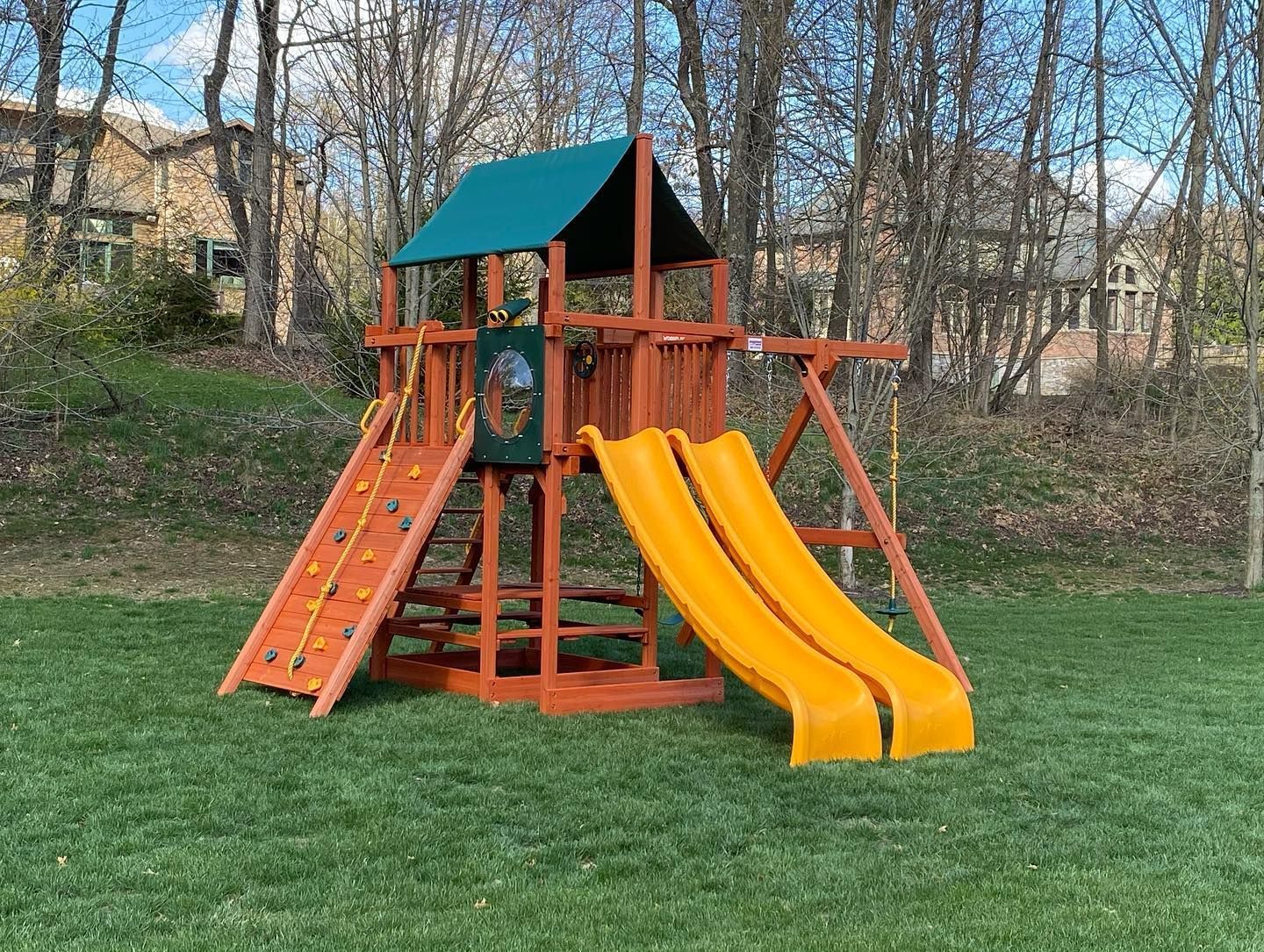 Orange playground with twin slides and climbing structure in a grassy park under bare trees