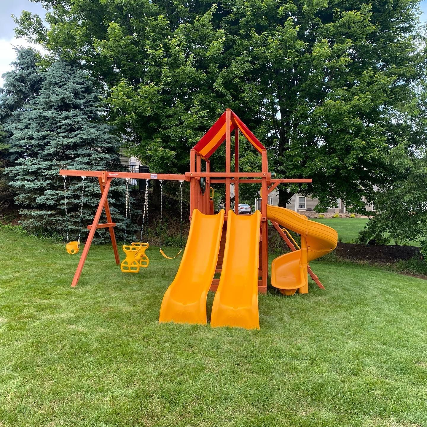Orange playground slide and swings on a grassy yard with trees in the background